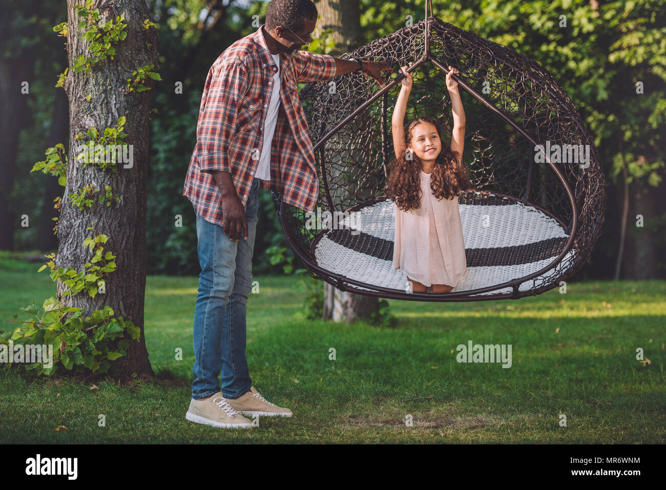 African American girl swinging sur fauteuil suspendu pendant que son grand-père debout près de Park Banque D'Images