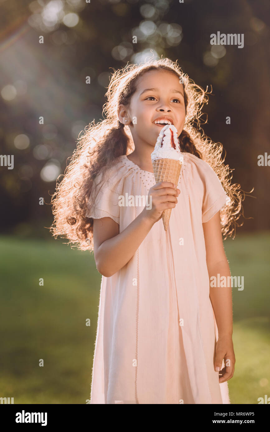 Heureux adorable african american girl eating ice cream cone dans la région de Park dans la lumière du soleil Banque D'Images