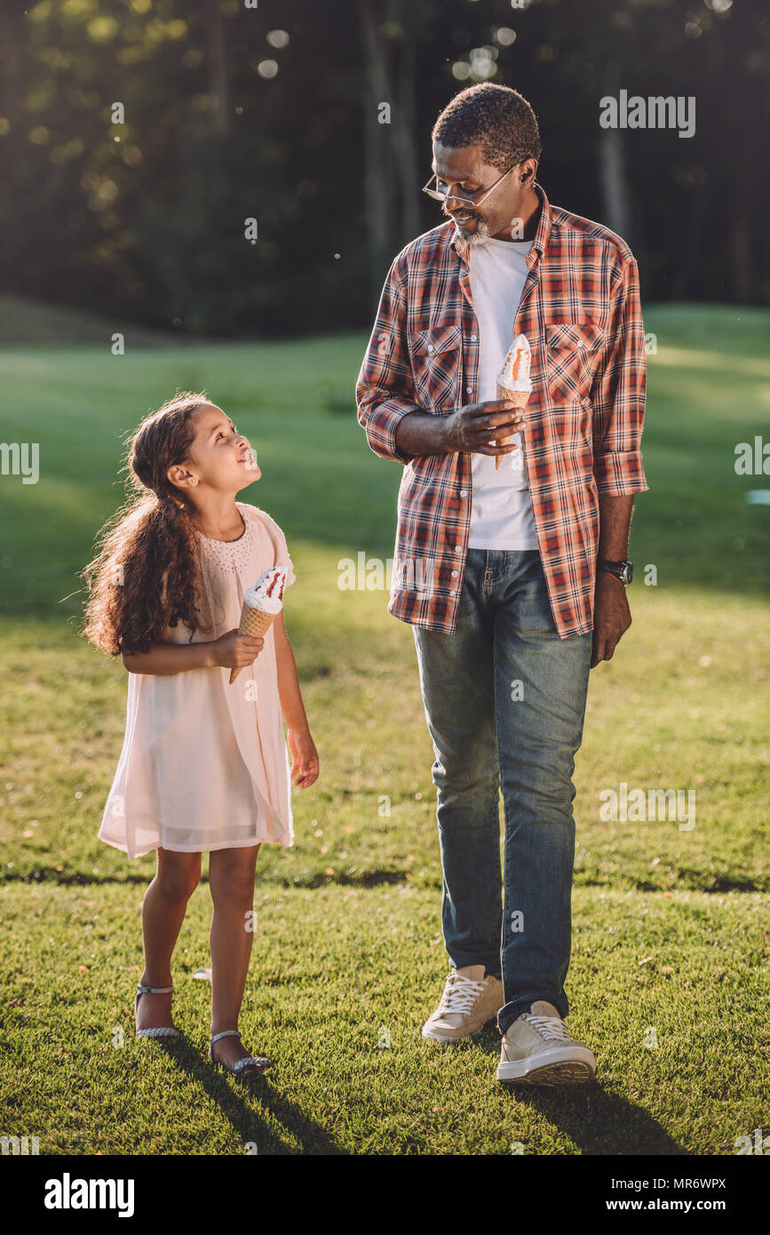 Smiling african american petite-fille et grand-père de manger de la crème glacée dans des cônes en marchant dans le parc Banque D'Images