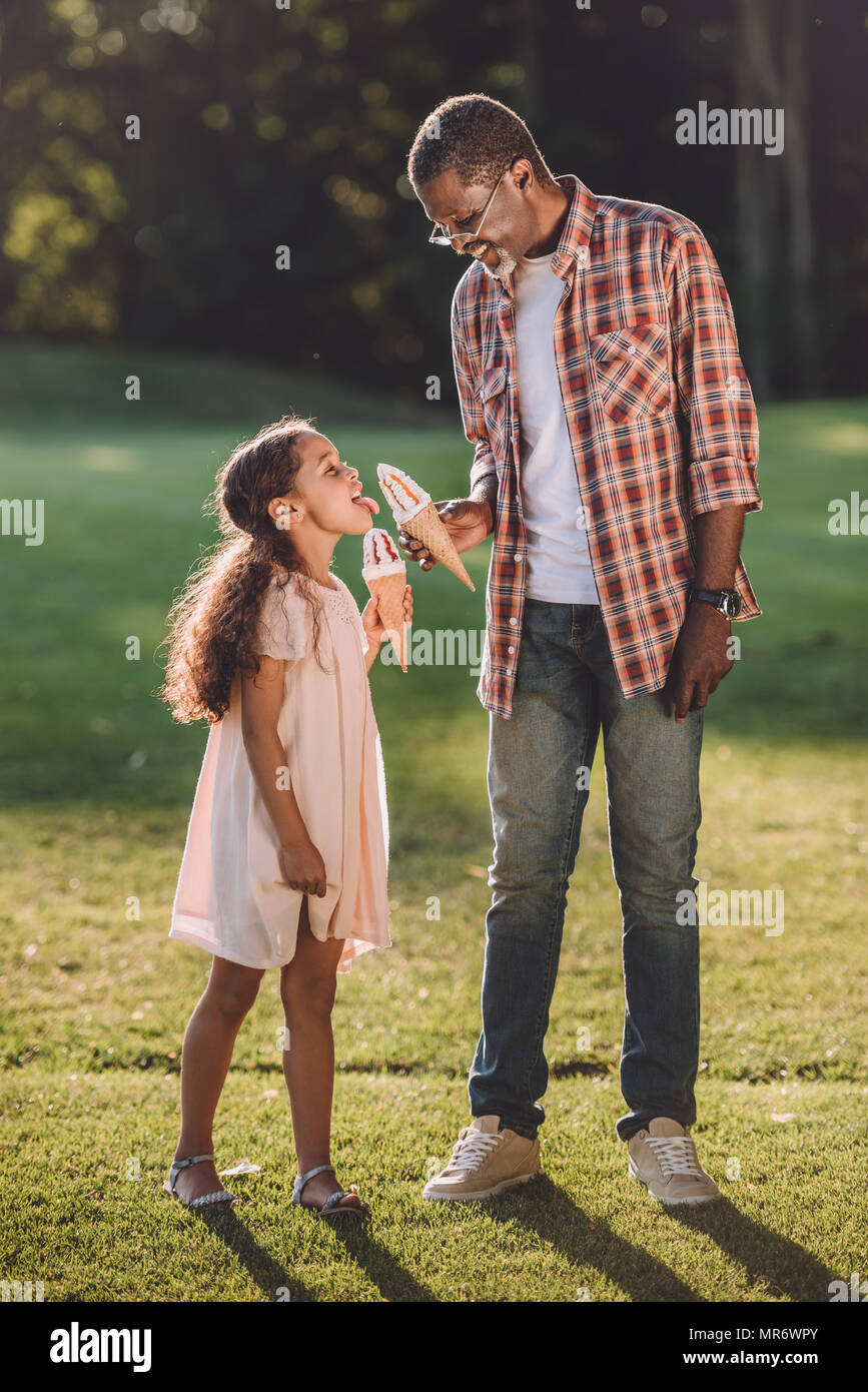 Happy african american girl et grand-père de manger de la crème glacée dans des cônes en marchant dans le parc Banque D'Images