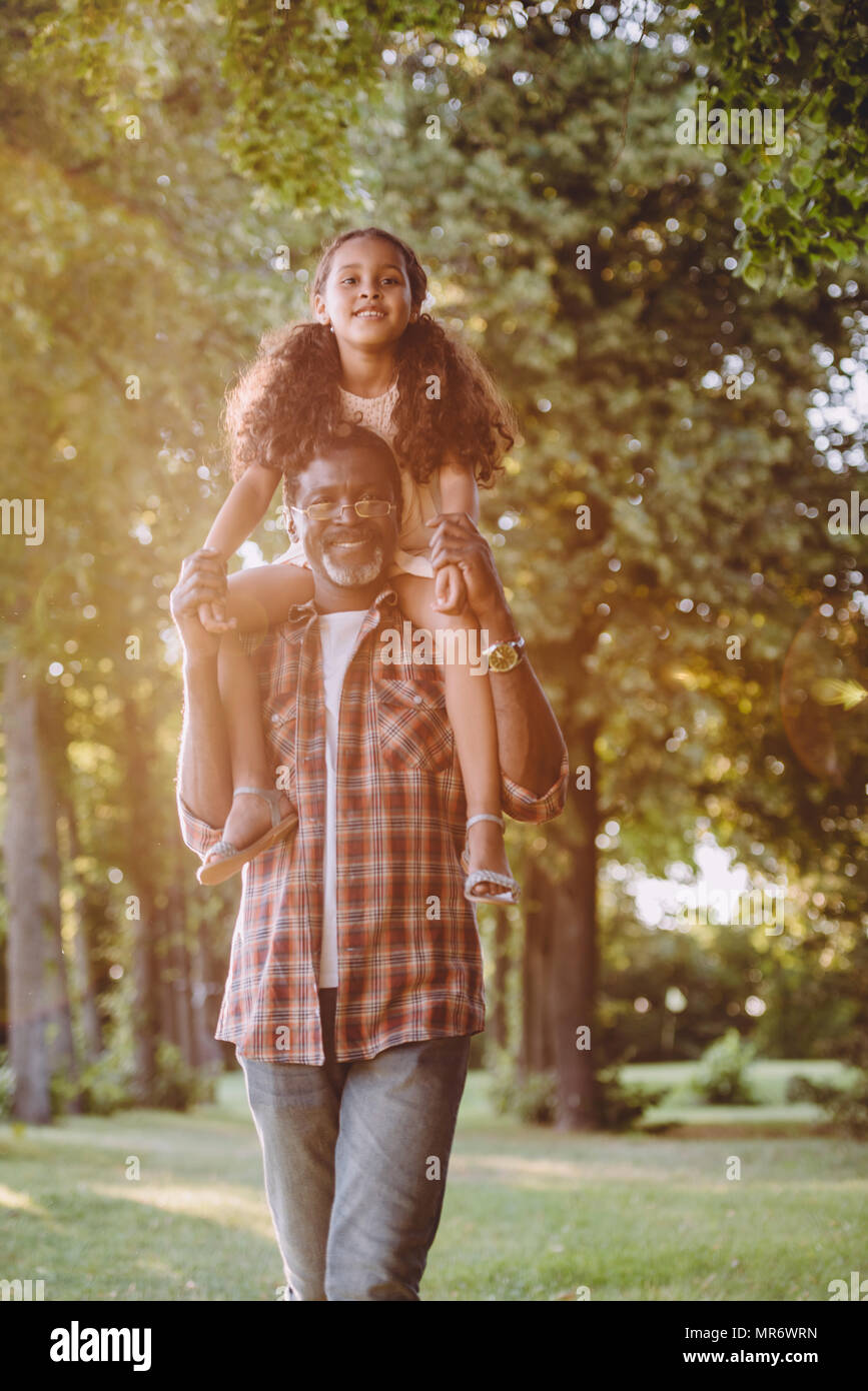 Smiling african american grand-père s'occuper sa petite fille sur les épaules en park Banque D'Images