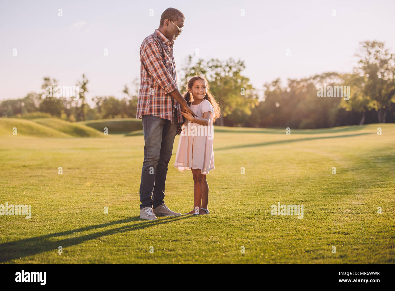 African American petite-fille et son grand-père tenant la main et debout sur pelouse verte Banque D'Images