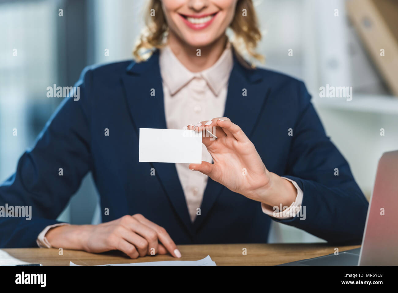 Portrait of smiling businesswoman showing blank carte de visite tout en restant assis sur le lieu de travail Banque D'Images