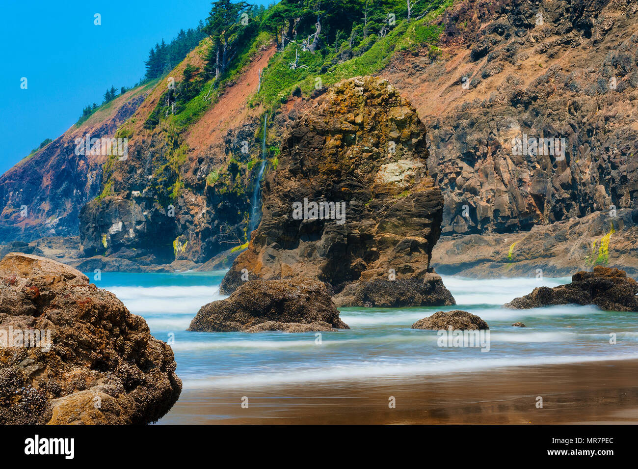 Scène de plage paysage où de grandes roches intertidales briser le surf entrant. Banque D'Images