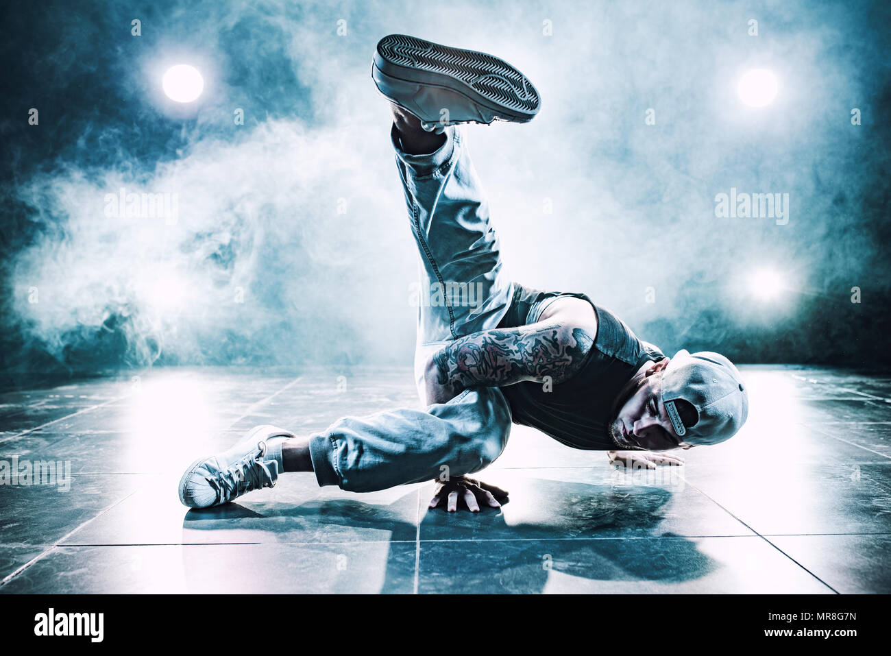 Jeune homme dans le break dance club avec des lumières et de la fumée. Tatouage sur le corps. Nuances de couleurs bleu. Banque D'Images