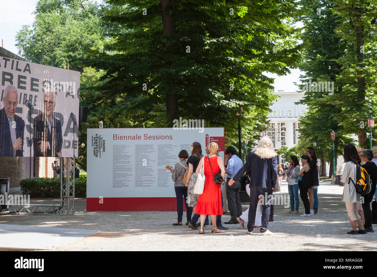 Venise, Vénétie, Italie. 26 mai 2018. Le jour de l'ouverture de la Biennale d'architecture de 2018 intitulé de l'espace disponible dans les Giardini Pubblici (Jardins Publics) Castello. Groupe de personnes regardant une rediffusion de la cérémonie de remise des prix et la présentation des prix à vie sous les arbres en face de la Biennale de Venise ou pavillon d'exposition. MLCpics Crédit/Alamy Live News Banque D'Images