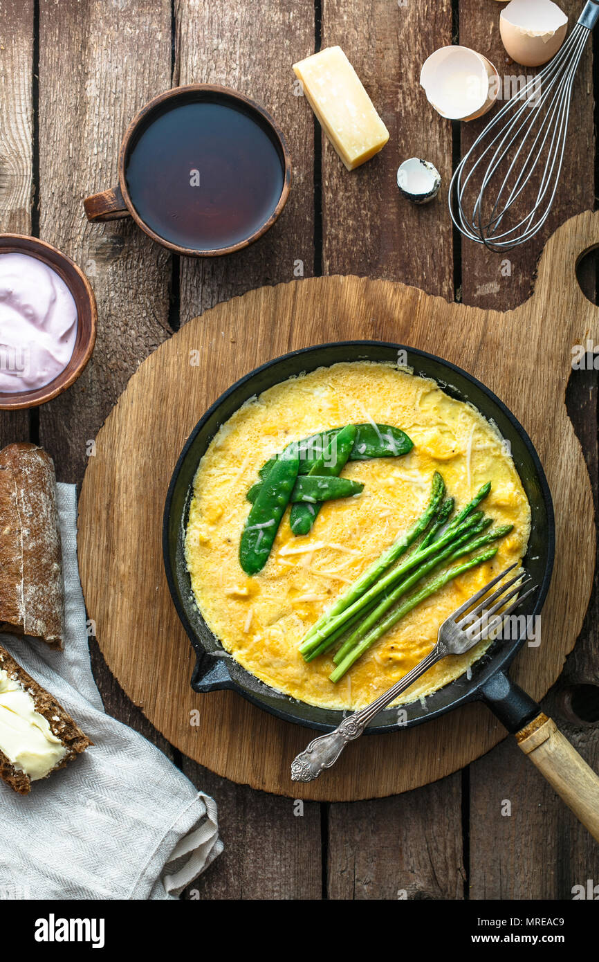 Omelette aux asperges vertes, pois sur poêle, vue de dessus, style rustique. Banque D'Images