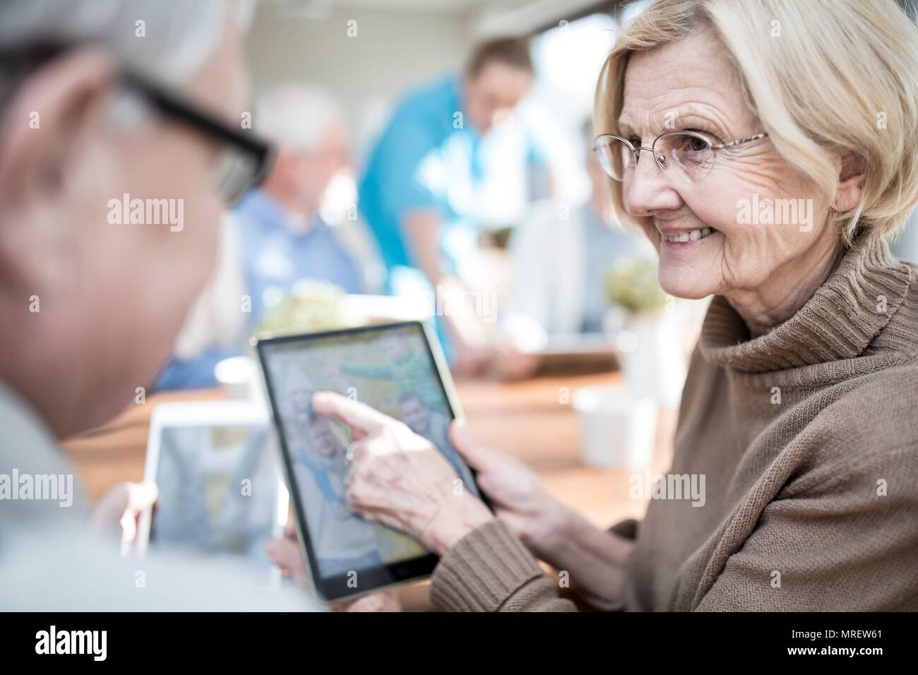 Des aînés à la recherche de photos sur tablette numérique en maison de soins. Banque D'Images