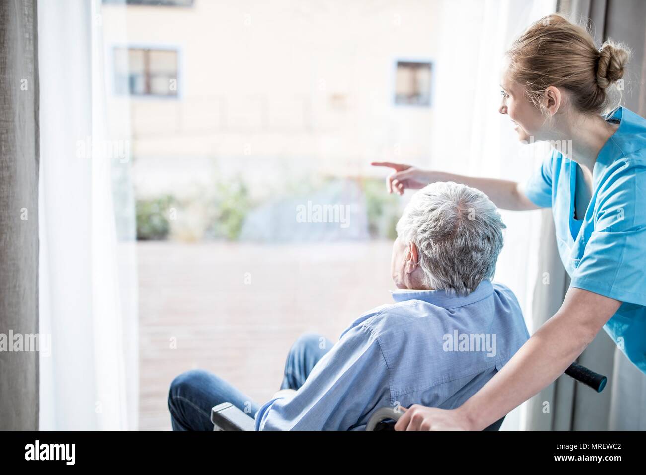 Senior man in wheelchair with care worker à la fenêtre de sortie. Banque D'Images