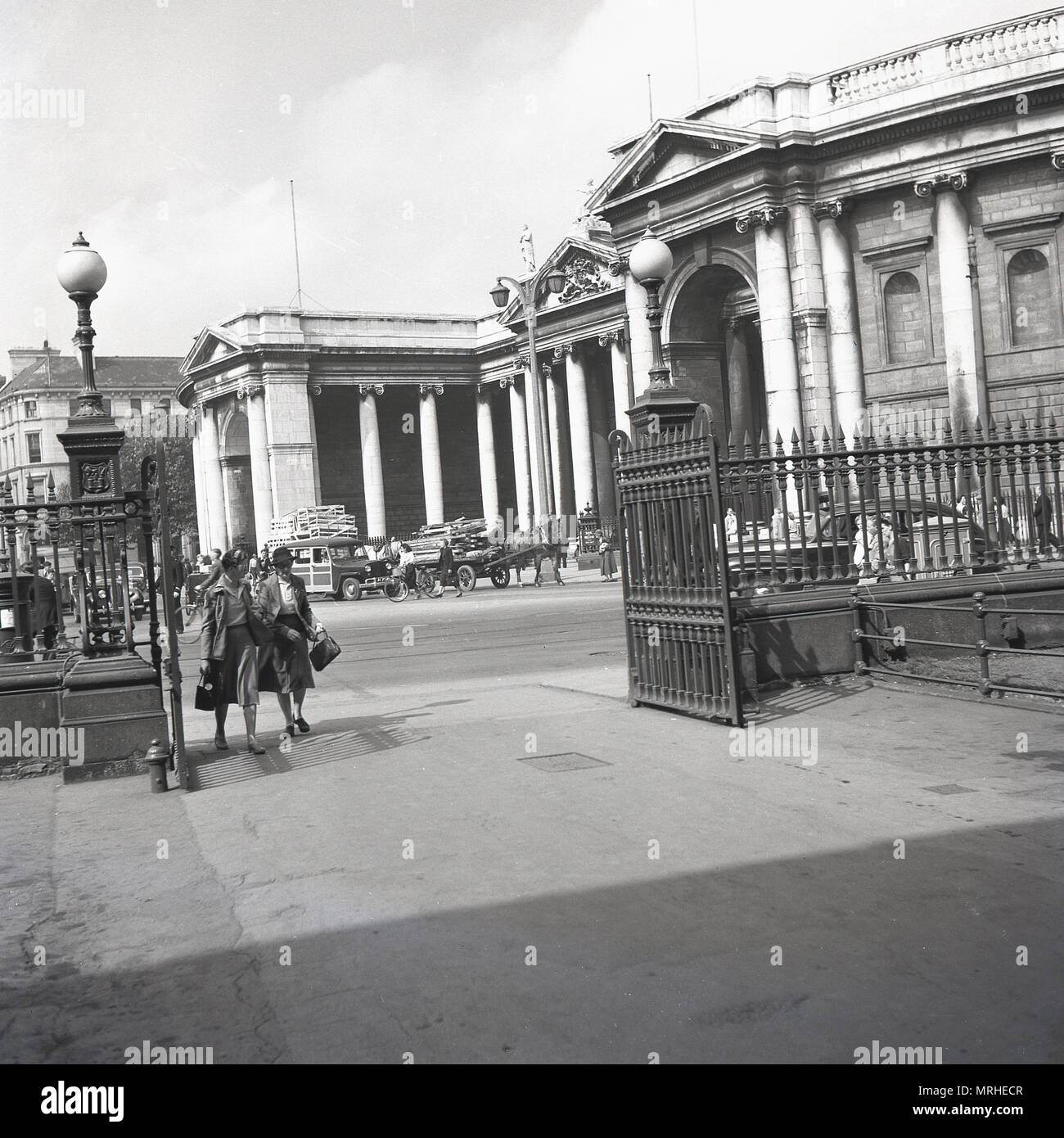 Années 1940, historique, deux dames marchent à travers l'entrée fermée ouverte de Trinity College, un campus universitaire historique à College Green, dans le centre-ville de Dublin, Irlande, Banque D'Images