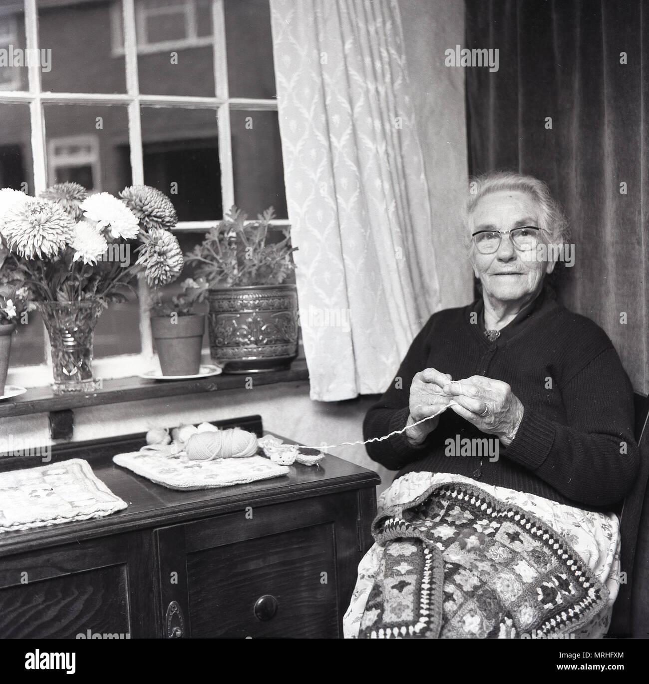 Années 1960, historique, dame âgée, dans un logement, assis à côté d'une fenêtre le kitting, England, UK. Banque D'Images