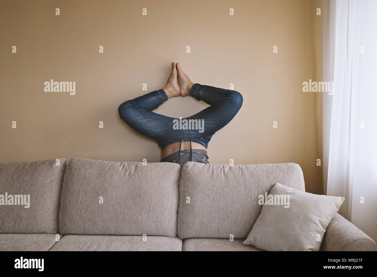 L'homme derrière la table handstanding beige, faisant du yoga et de nettoyage de printemps, concept de soins mobilier Banque D'Images