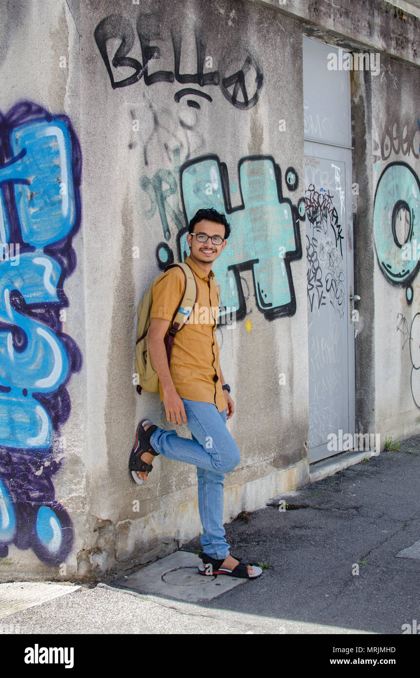 Portrait de jeune adulte jeune Indien posant contre un mur de graffiti avec sac à dos, à la recherche vers la caméra. Banque D'Images