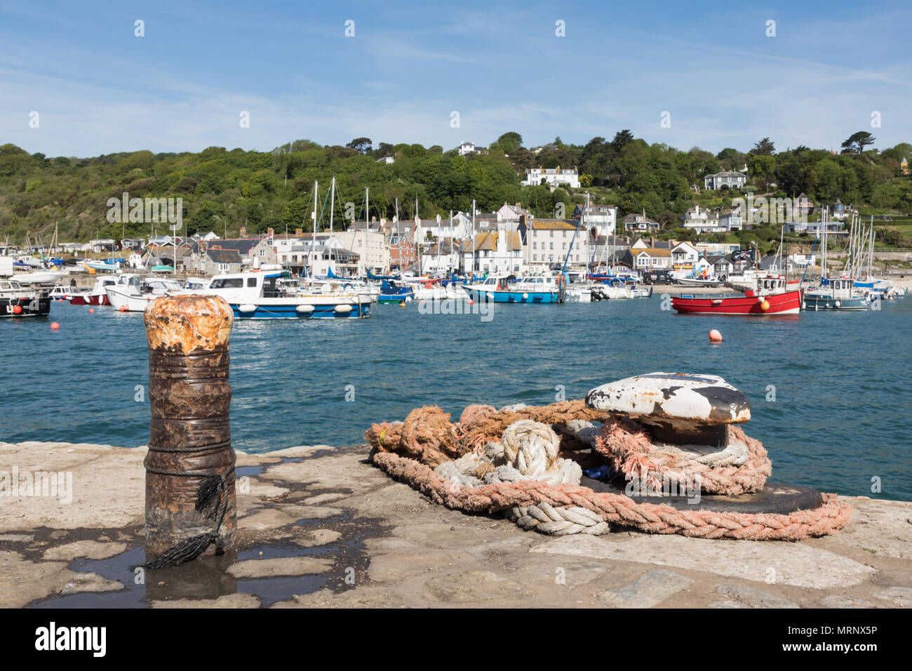 Les petits bateaux à l'ancre sur une mer bleue à Lyme Regis port. Après un fer à repasser et d'acier ne sont enroulés à l'avant-plan. Les maisons sont éclairées par en arrière-plan. Banque D'Images