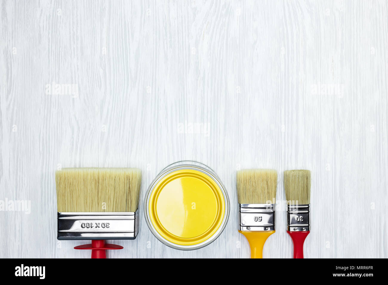 Différents pinceaux et peinture jaune peut sur fond gris en bois 24. Vue de dessus Banque D'Images