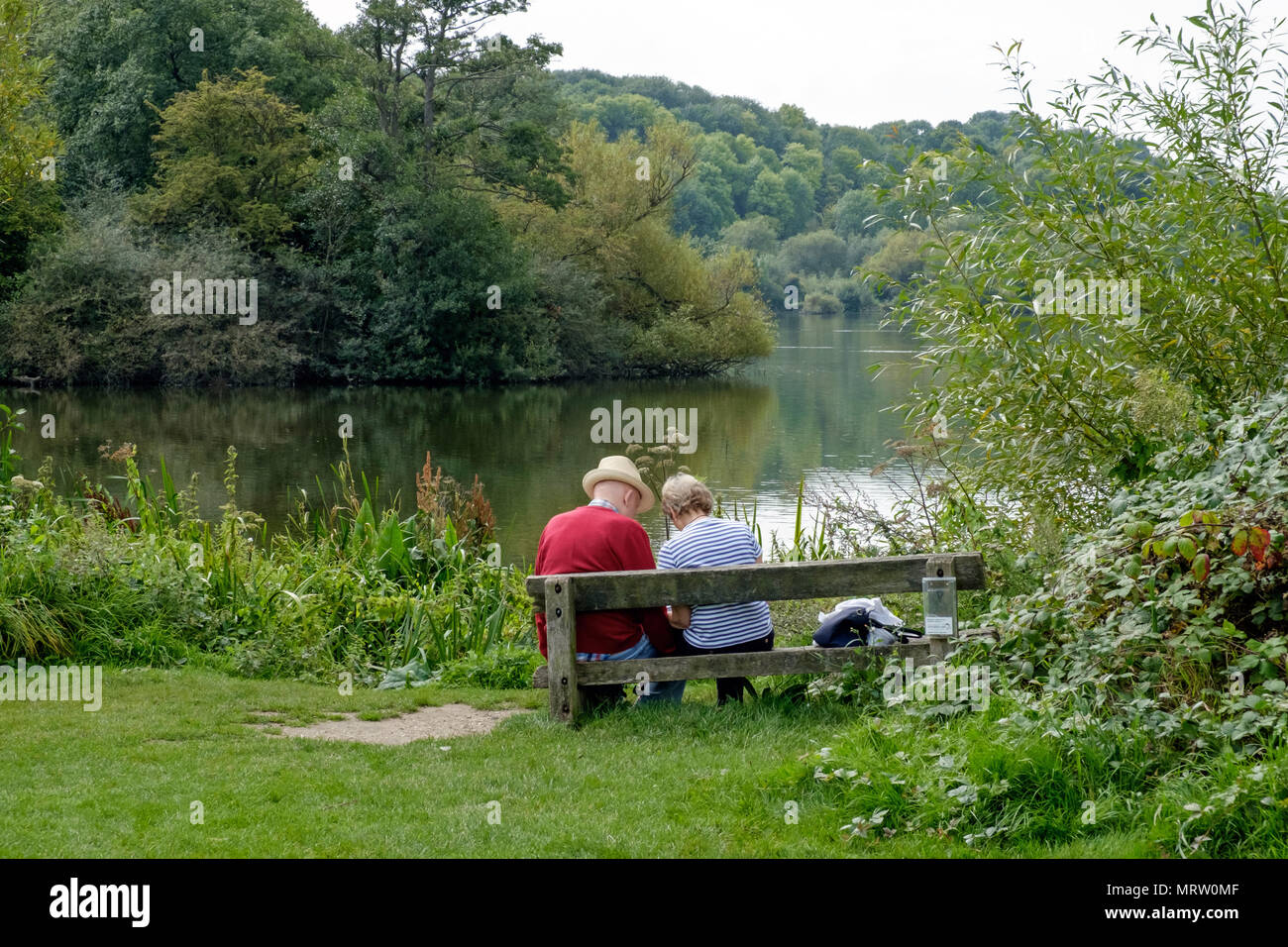 Couple de personnes âgées s'asseoir sur un banc à Rickmansworth Aquadrome, Hertfordshire, Angleterre du Sud-Ouest, en face de l'eau entouré par la nature. Paysage. July2017 Banque D'Images
