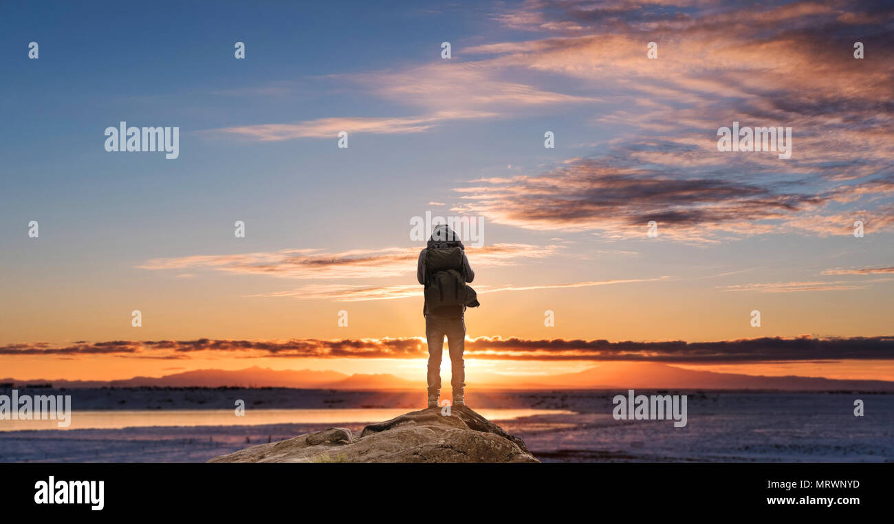 Sac à dos avec un homme debout sur le rocher profitant de lever du soleil le matin Banque D'Images