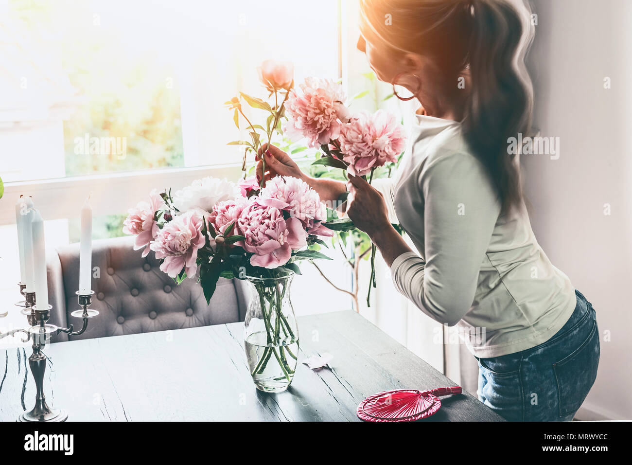 Les femmes attirantes organiser pivoines bouquet en vase en verre sur la table à fenêtre dans la salle de séjour. Style de vie. Happy Home Banque D'Images