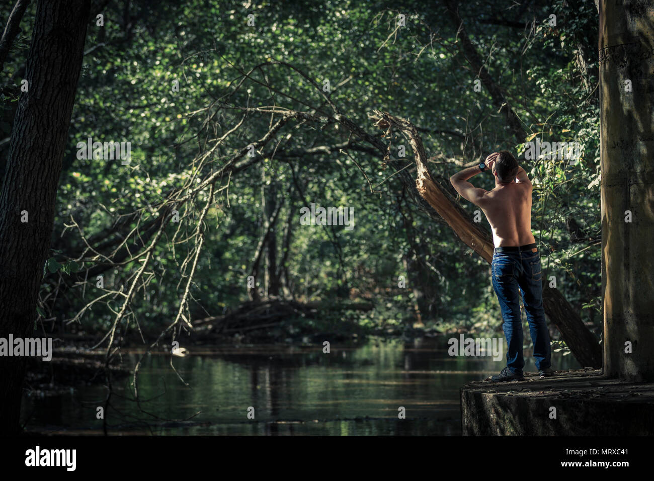 Vue arrière de l'homme torse nu en jeans comité permanent et de crier sur fond d'étang et arbres verts Banque D'Images