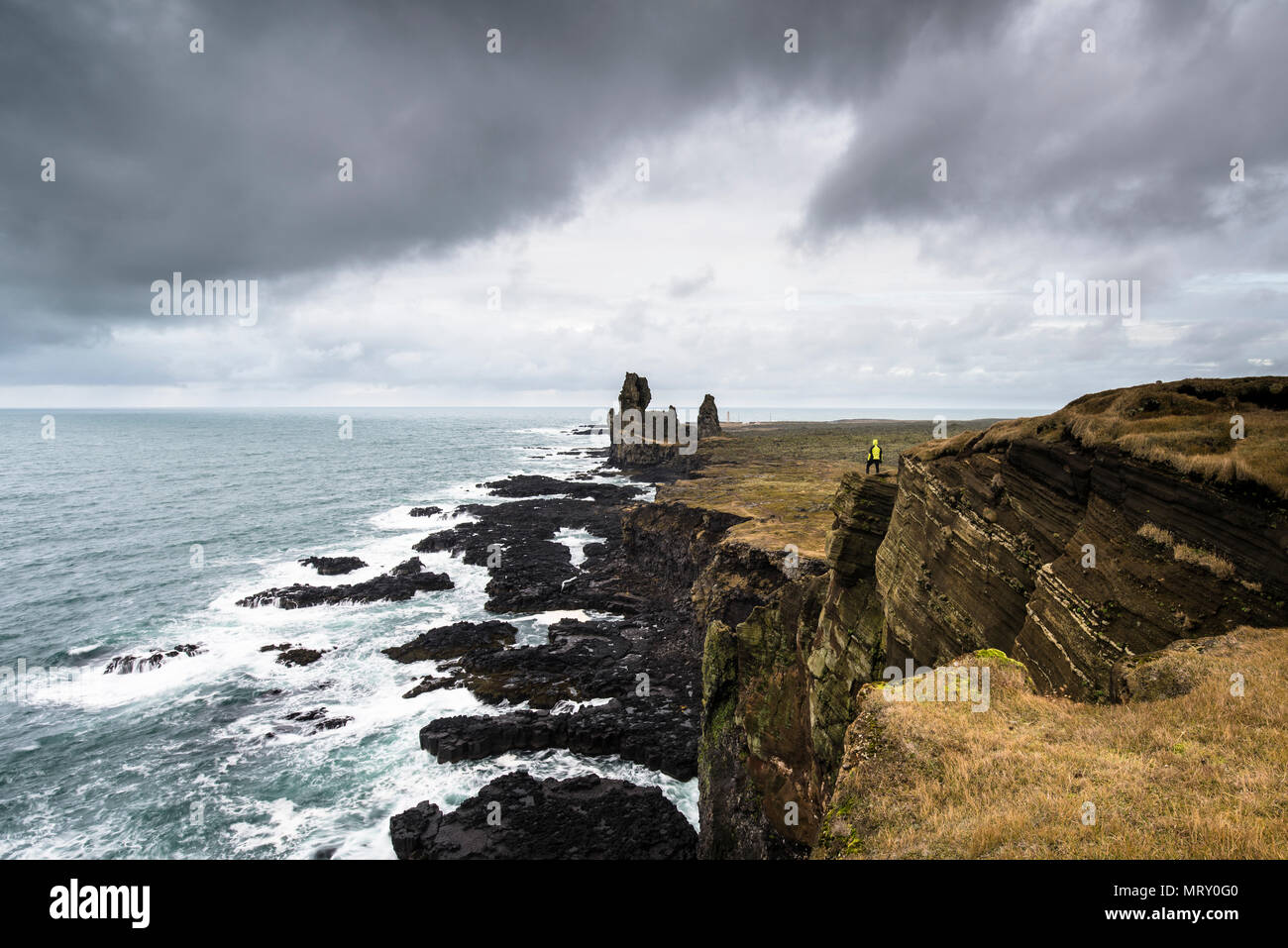 Péninsule de snæfellsnes, dans l'ouest de l'Islande, Islande. Londrangar pile la mer et falaises côtières. Un homme est debout sur la falaise Banque D'Images