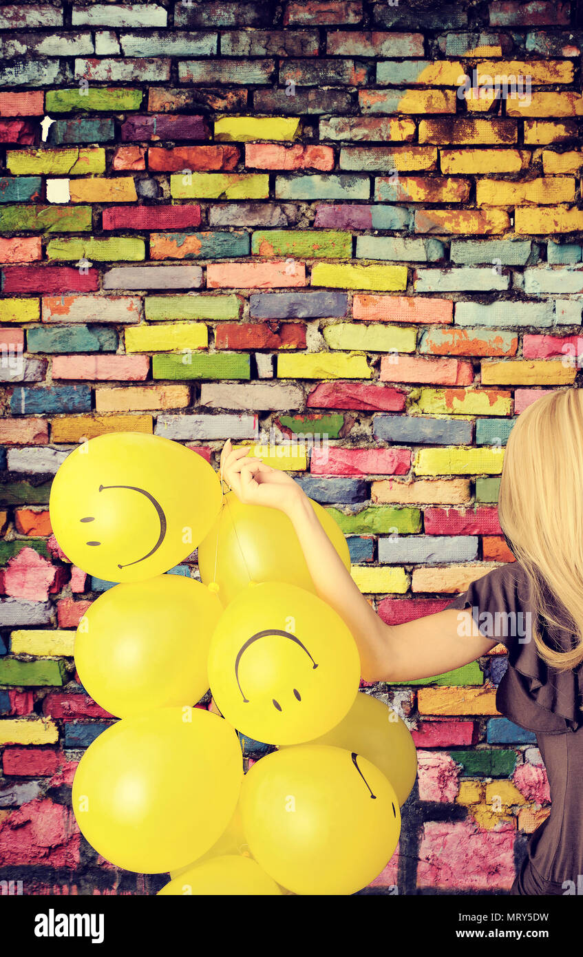 Jeune femme avec des ballons smiley contre un mur de briques colorées Banque D'Images