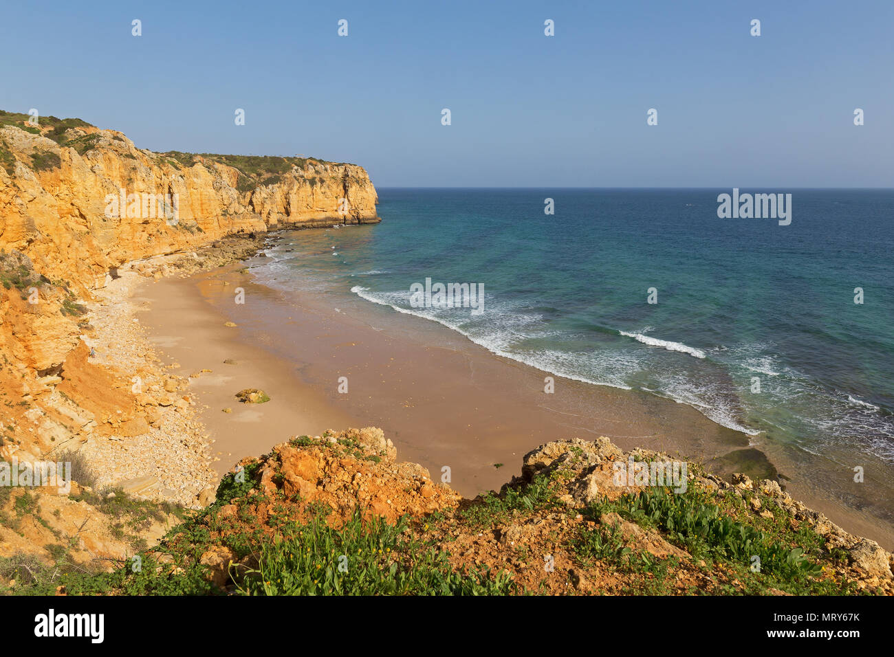 Plage de sable de l'Océan Atlantique formé entre deux falaises au coucher du soleil, Algarve, Portugal. Les vagues sont roulant sur une plage de sable isolée. Banque D'Images