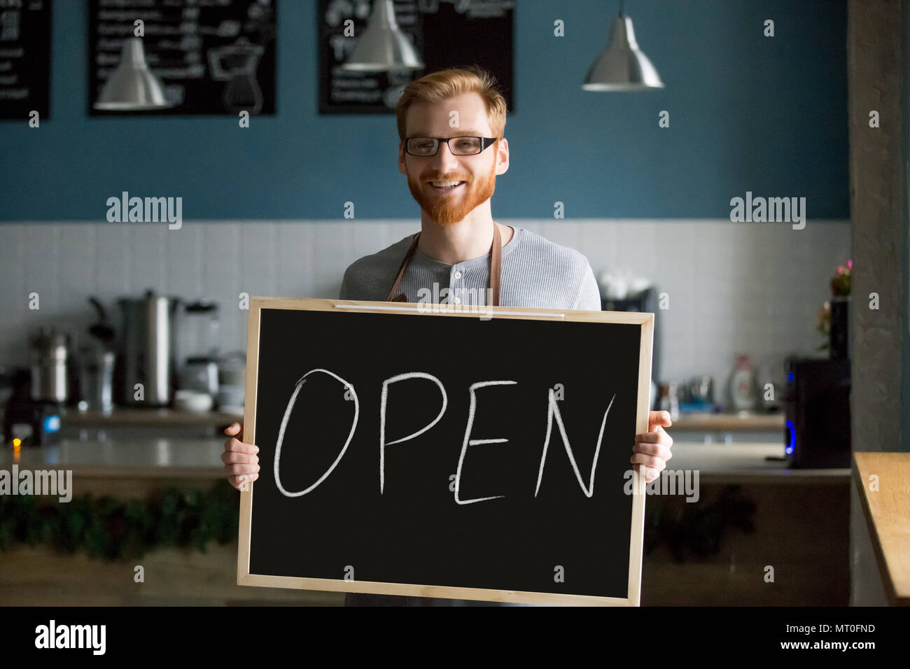 Redhead smiling man holding open sign invitant à nouveau café Banque D'Images