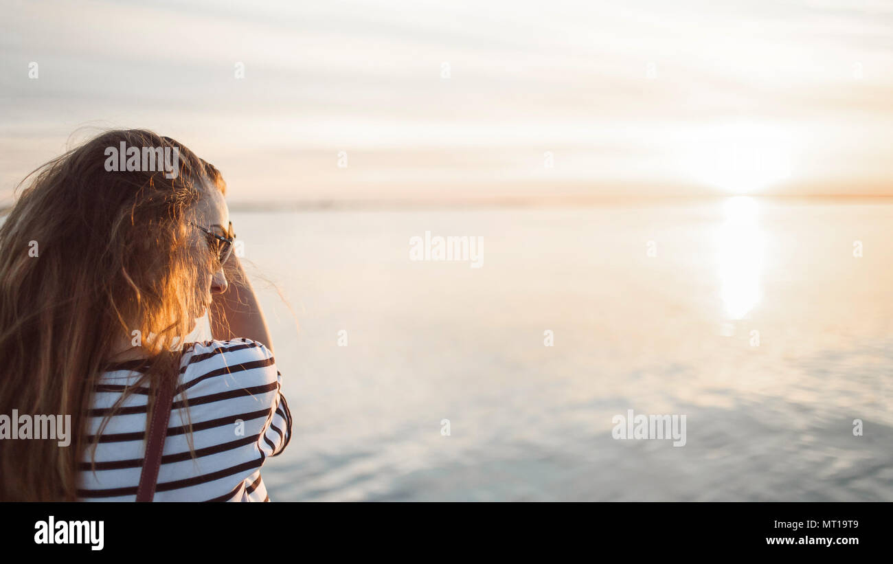 Une jeune femme cherche à le coucher du soleil sur une mer ou une rivière avec de beaux reflets de soleil dans l'eau douce. Summer Joy, insouciant concept. Copier l'espace. Banque D'Images