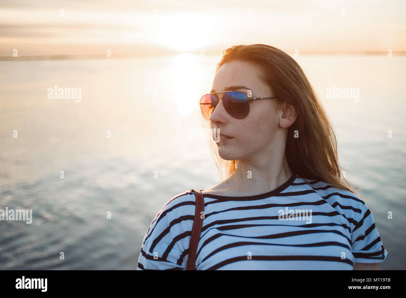 Une jeune femme cherche à le coucher du soleil sur une mer ou une rivière avec de beaux reflets de soleil dans l'eau douce. Banque D'Images