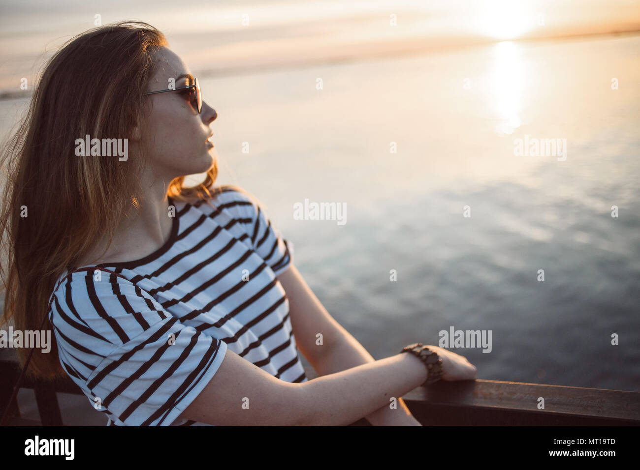 Une jeune femme cherche à le coucher du soleil sur une mer ou une rivière avec de beaux reflets de soleil dans l'eau douce. Soft focus. Banque D'Images
