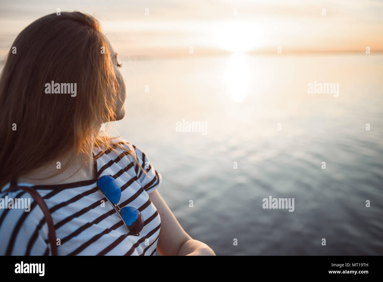 Une jeune femme cherche à le coucher du soleil sur une mer ou une rivière avec de beaux reflets de soleil dans l'eau douce. Banque D'Images