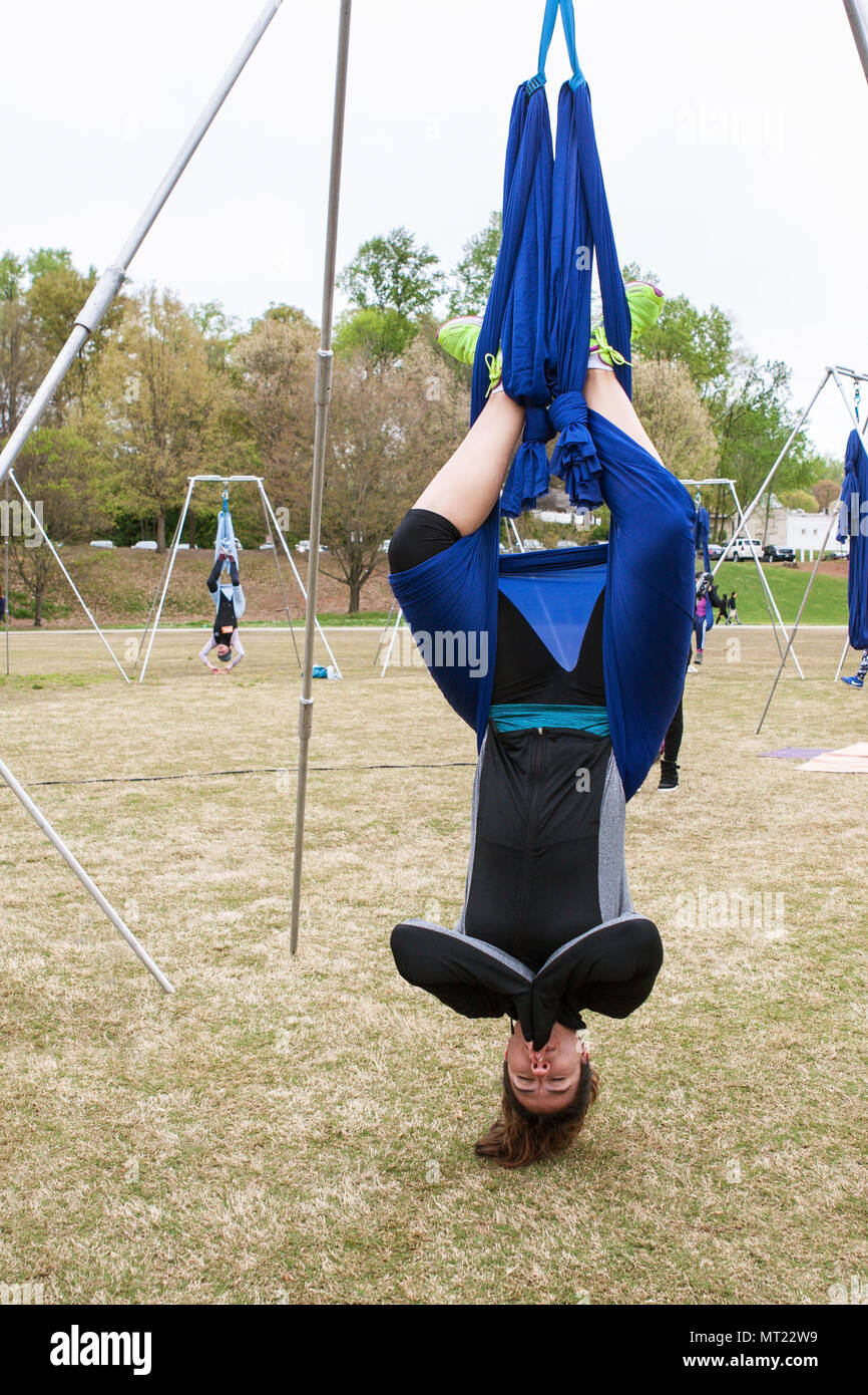 Une femme est suspendu à l'envers à l'aide de tissu attaché à des poteaux, alors qu'elle prend part à une classe de yoga dans la région de Piedmont Park à Atlanta, GA, le 8 avril 2018. Banque D'Images