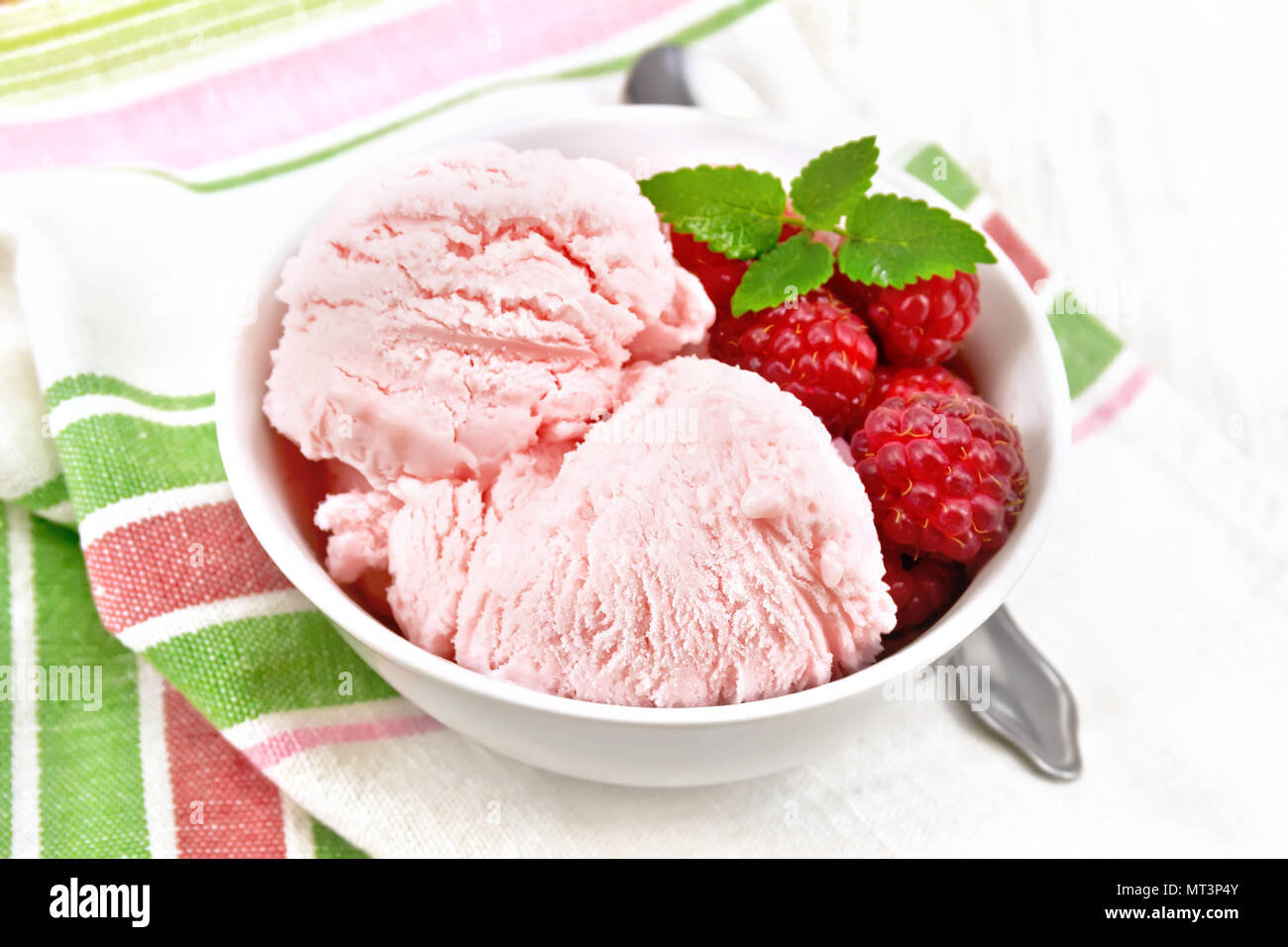 La crème glacée à la framboise rouge et menthe baies en blanc bol, une cuillère sur serviette sur l'arrière-plan de planche de bois Banque D'Images