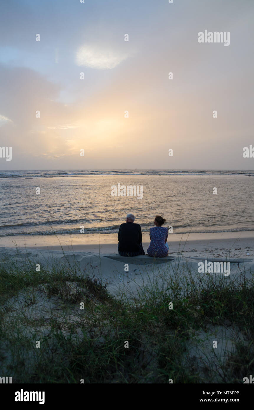 Unidentifieable moyen age couple sitting on beach à la recherche sur la mer au coucher du soleil, le Sénégal, l'Afrique Banque D'Images
