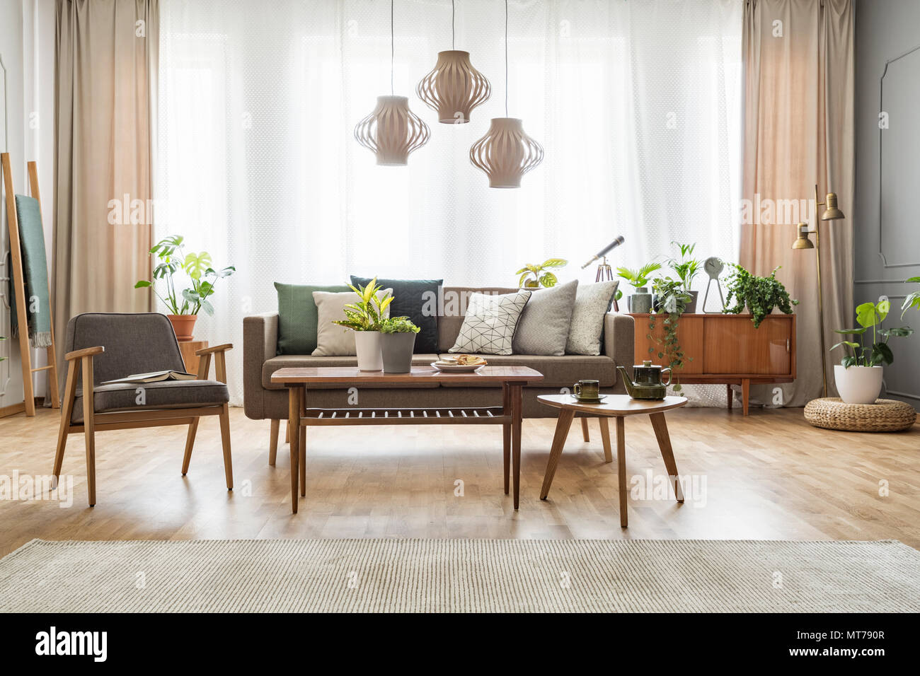 Fauteuil gris à côté du canapé et table en bois avec des coussins en télévision intérieur avec des tentures et des lampes. Photo réelle Banque D'Images