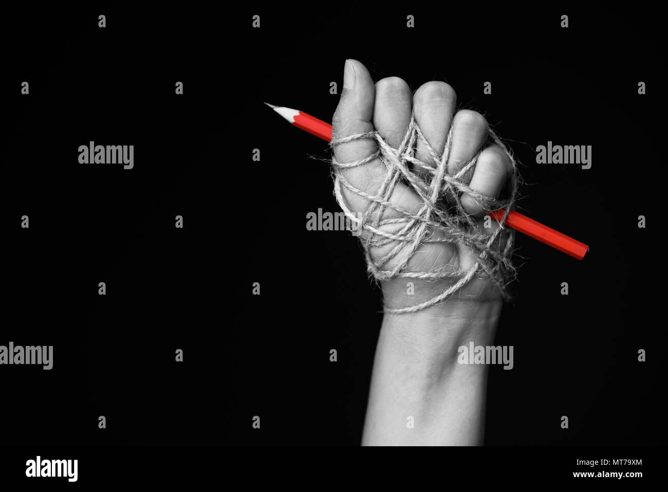 La main avec crayon rouge attaché avec de la corde, illustrant l'idée de la liberté de la presse ou la liberté d'expression sur fond sombre en bas. Banque D'Images