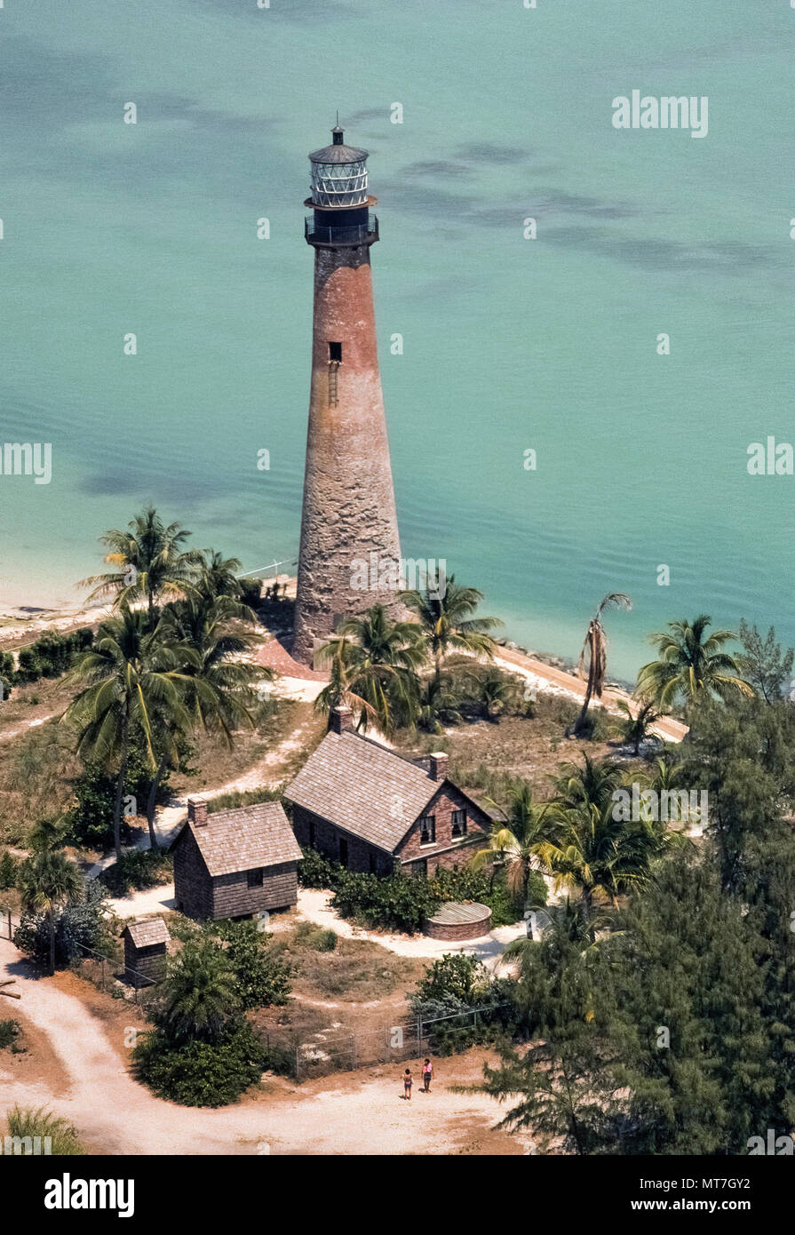Cette vue aérienne montre comment le phare historique de 1825 dans le projet de loi Baggs Cape Florida State Park en 1976 avant sa restauration actuelle lorsque l'original à la maçonnerie était couvert de stuc blanc à l'extrémité sud de Key Biscayne dans le comté de Miami-Dade, en Floride, aux États-Unis. Une balise de navigation au sommet de la 95-foot-tall (29 mètres) monument phare a été rallumée en 1996 pour célébrer le centenaire de Miami. Une réplique de l'habitation utilisée par le gardien de la Cape Florida Light (au premier plan) est devenue un musée retraçant l'histoire maritime de l'état. Photo historique. Banque D'Images Cette vue aérienne montre comment le phare historique de 1825 dans le projet de loi Baggs Cape Florida State Park en 1976 avant sa restauration actuelle lorsque l'original à la maçonnerie était couvert de stuc blanc à l'extrémité sud de Key Biscayne dans le comté de Miami-Dade, en Floride, aux États-Unis. Une balise de navigation au sommet de la 95-foot-tall (29 mètres) monument phare a été rallumée en 1996 pour célébrer le centenaire de Miami. Une réplique de l'habitation utilisée par le gardien de la Cape Florida Light (au premier plan) est devenue un musée retraçant l'histoire maritime de l'état. Photo historique. Banque D'Images