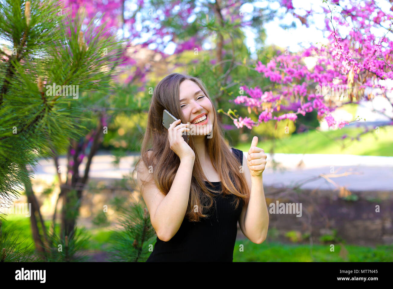 Jolie fille parler par smartphone et showing Thumbs up in spring park. Banque D'Images