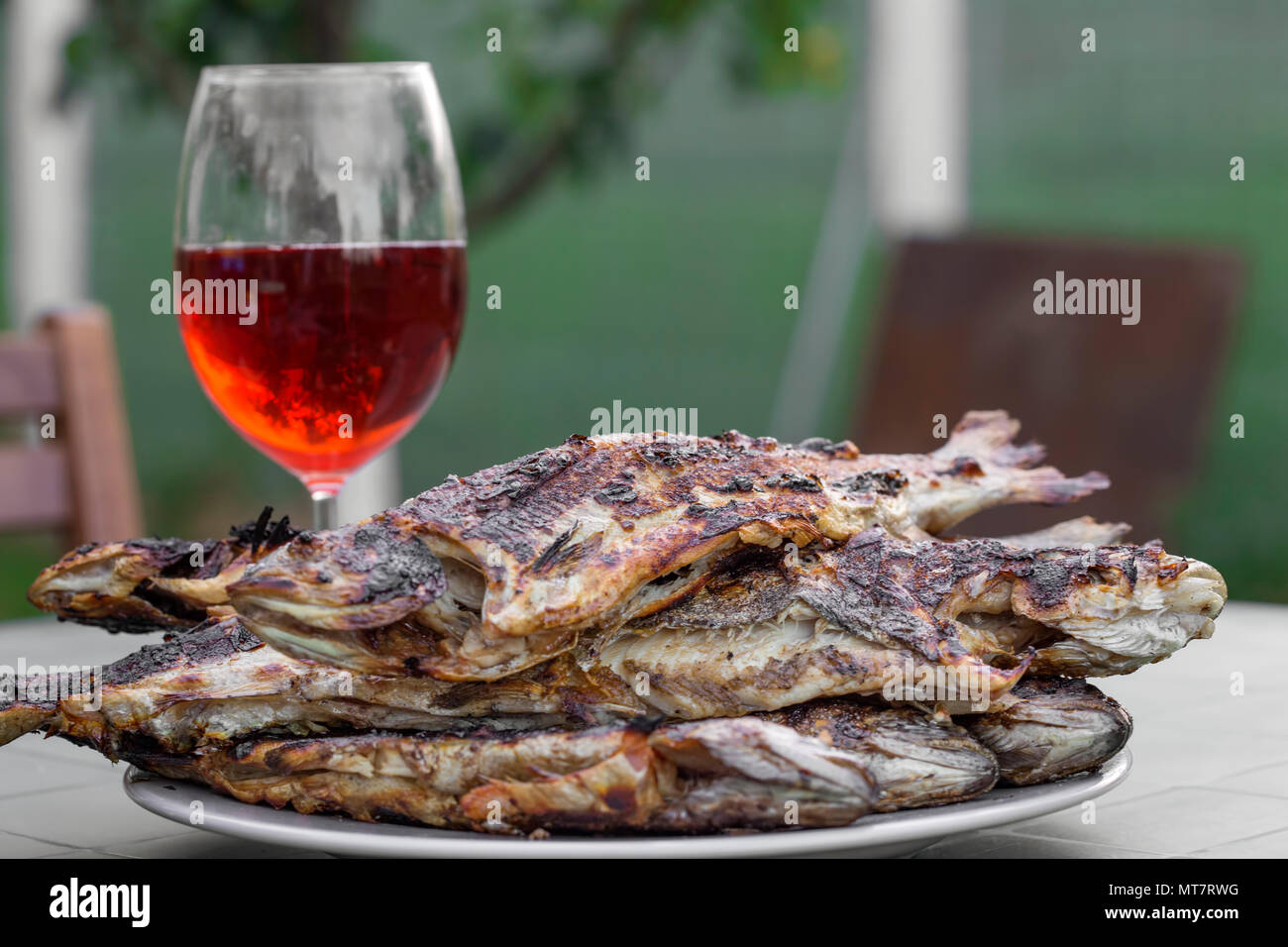 Tas de truite frais grillé sur plaque et un verre rempli de vin rouge en arrière-plan- prêt à manger Banque D'Images