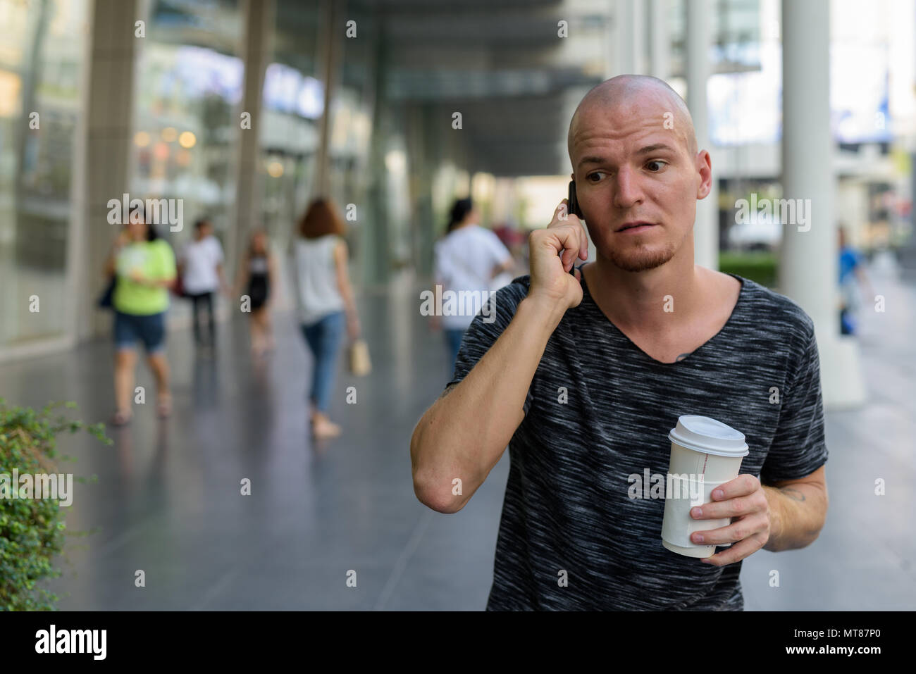 Beau jeune homme chauve holding paper Coffee cup tout en parlant o Banque D'Images