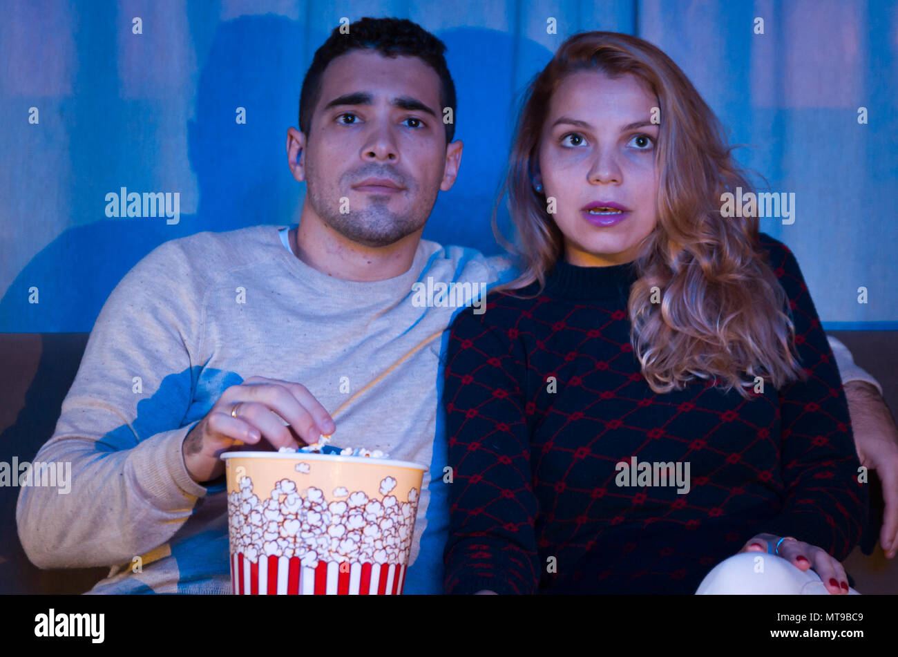 Jeune couple regardant thriller film dans une pièce sombre avec des pop-corn sur canapé attention entièrement Banque D'Images