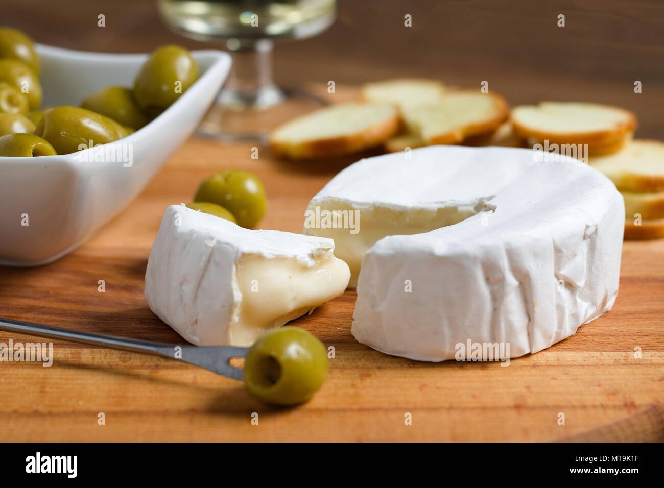 Fromage à pâte molle à croûte blanche (camembert ou brie) sur planche de bois avec des tranches de pain grillées, olives et vin blanc Banque D'Images
