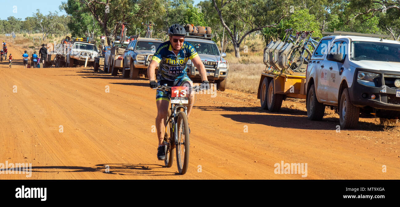 Un cycliste en vtt équitation passé un convoi de véhicules de soutien sur la Gibb River Road de saleté sur le Défi 2018 Gibb, Kimberley WA, Australie. Banque D'Images