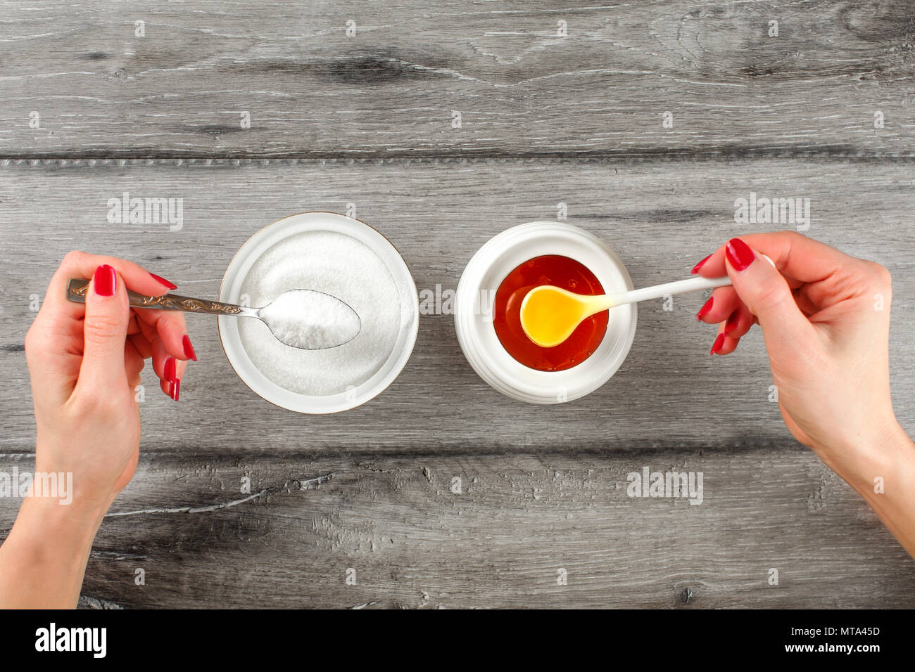 Vue supérieure de la jeune femme sur les mains avec des clous rouges, holding spoon plein de sucre et de miel dans un autre côté. Vs Sucre Miel concept. Banque D'Images