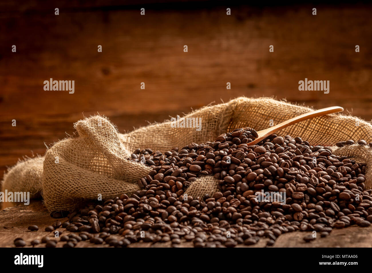 Vue rapprochée de sac de grains de café frais déversé avec cuillère en bois sur fond brun Banque D'Images