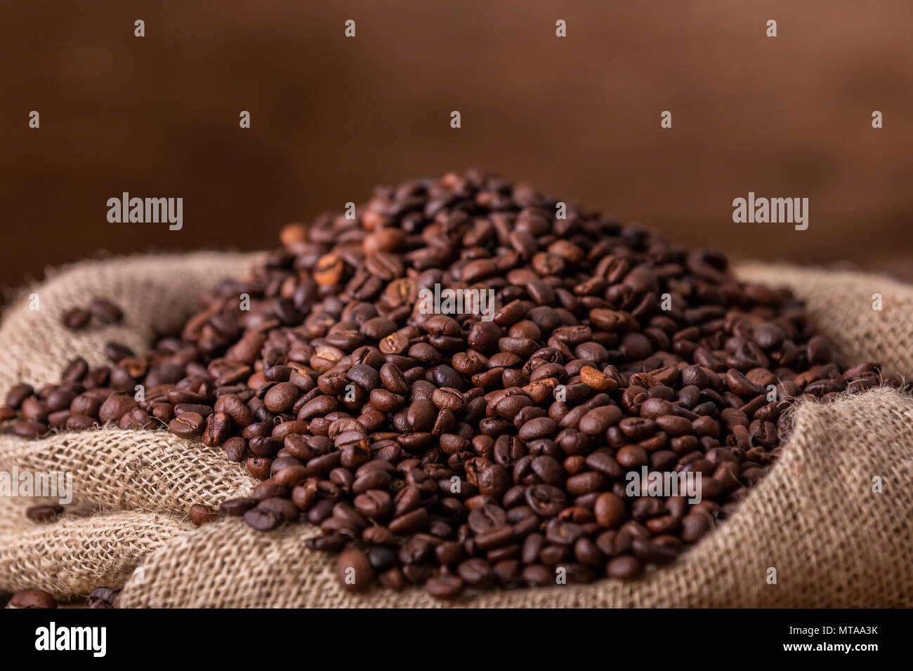 Sac de grains de café frais déversé sur fond de bois brun Banque D'Images