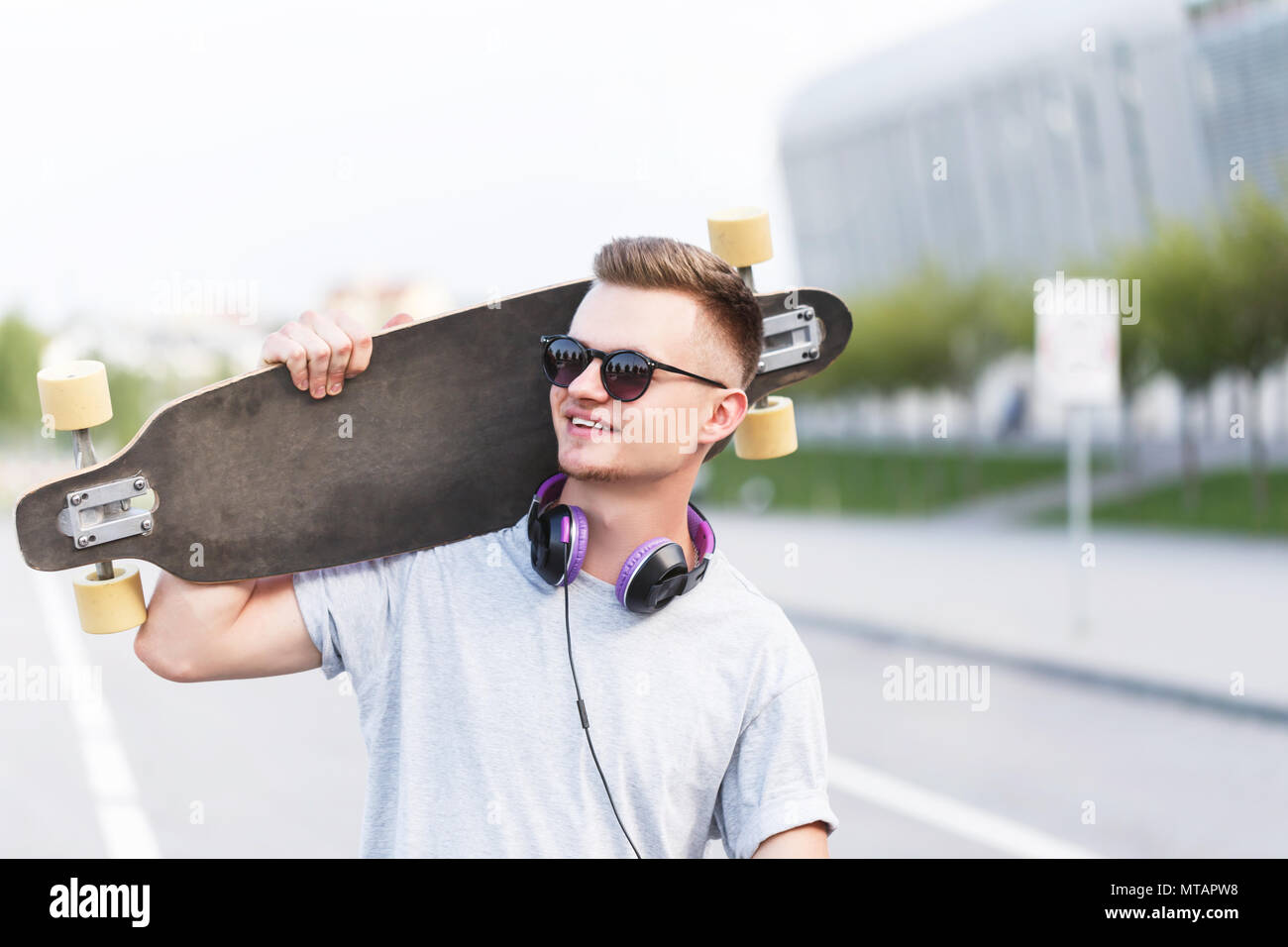 Skateur professionnel vêtu de gris t-shirt et lunettes de soleil avec des  écouteurs est titulaire sur l'épaule de longboard on city street Photo  Stock - Alamy
