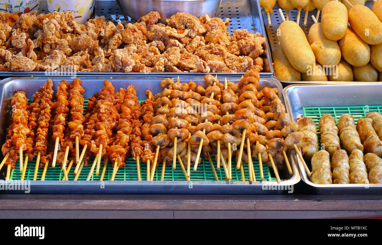 Un homme vend des brochettes de viande de poulet frit, et les chiens de maïs Banque D'Images