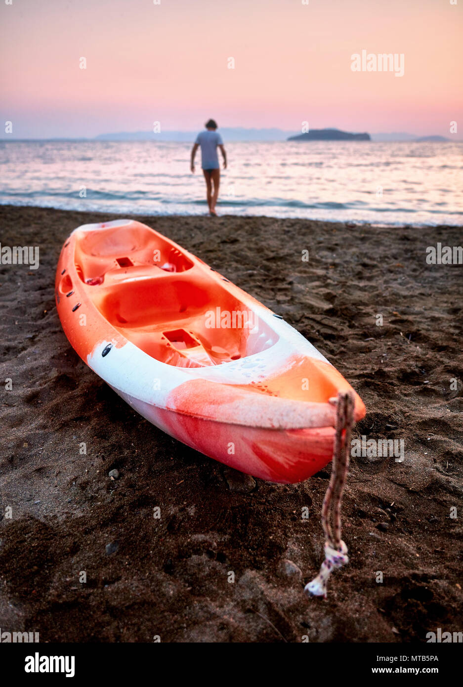 Une orange canoë sur la plage et un homme qui marche vers la mer Banque D'Images