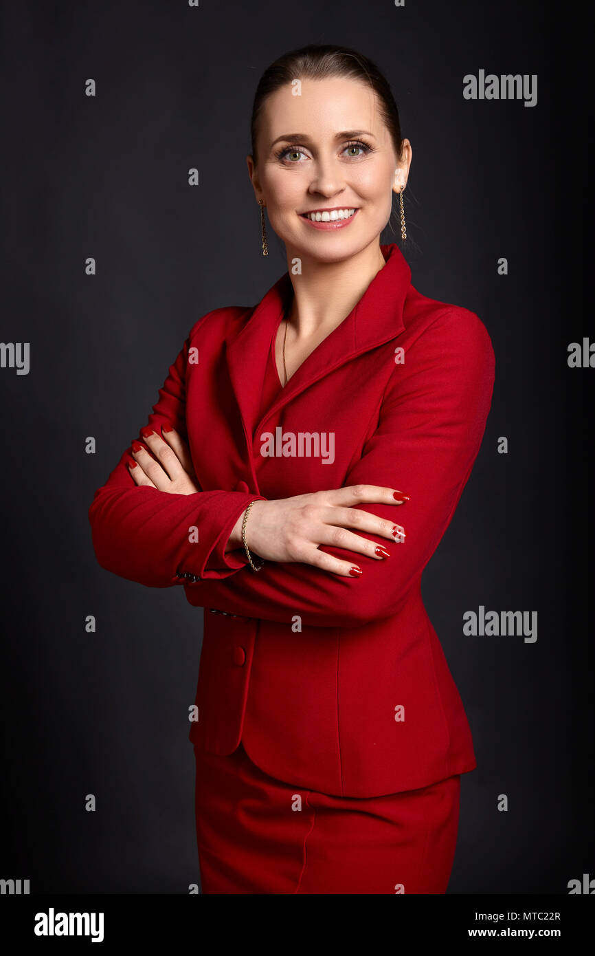 Portrait de jeune femme d'affaires élégante en rouge jupe blanc avec sourire et bras croisés, sur fond noir. Banque D'Images